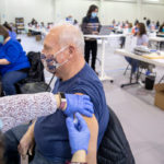 A man wearing a face mask gets a vaccine in his left arm at a vaccine clinic