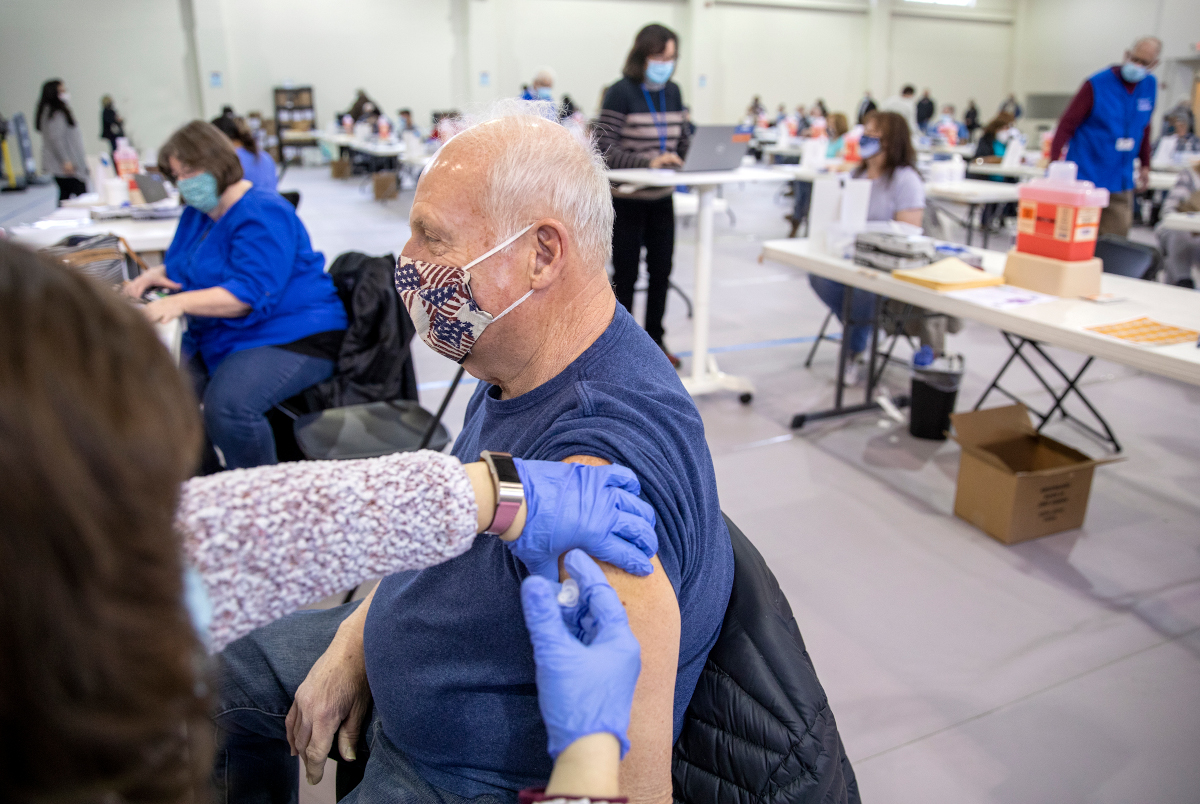 A man wearing a face mask gets a vaccine in his left arm at a vaccine clinic