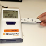 A hand inserts a tab into the side of a box with a digital display.