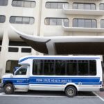 Bus with the words Penn State Health Shuttle printed on the side parked outside a hospital entrance.