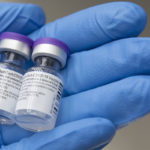 A close-up of a gloved hand cradling two vials of Pfizer-BioNTech COVID-19 Vaccine.