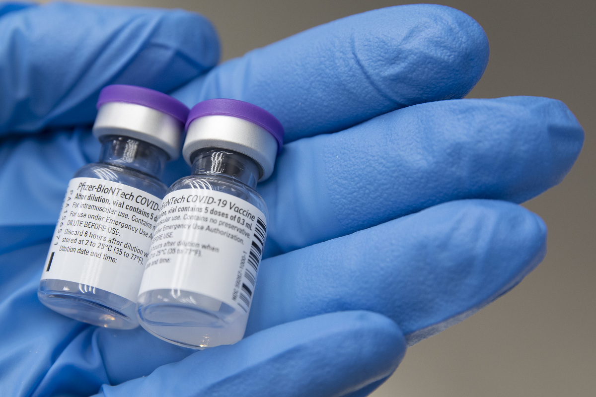 A close-up of a gloved hand cradling two vials of Pfizer-BioNTech COVID-19 Vaccine.