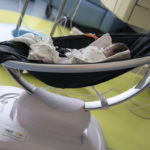 An infant takes a nap in a Mamaroo device, which is resting on the floor of a hospital room.