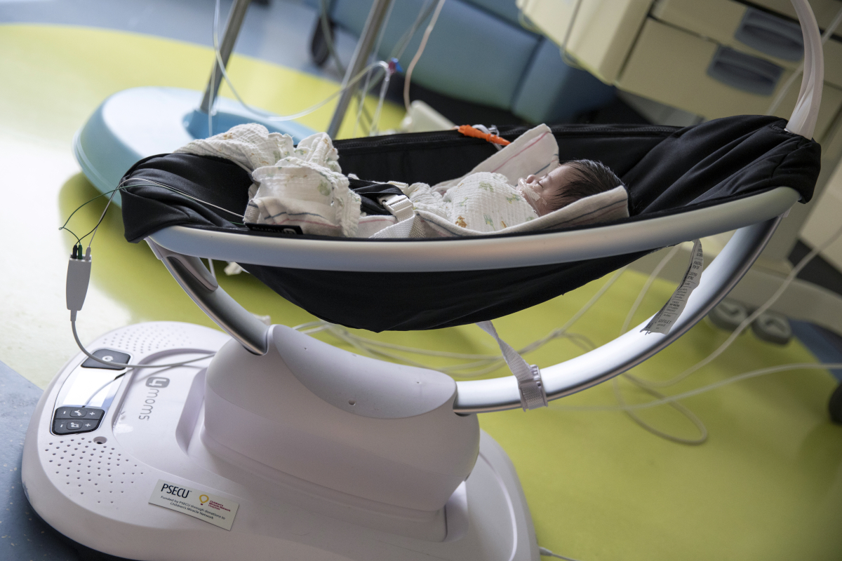An infant takes a nap in a Mamaroo device, which is resting on the floor of a hospital room.