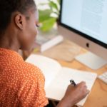Woman sitting at desk taking notes in front of her computer