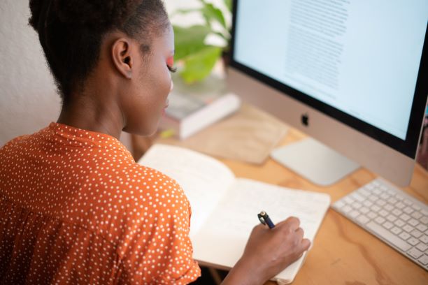 Woman sitting at desk taking notes in front of her computer