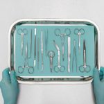 Gloved hands hold a tray of medical instruments.