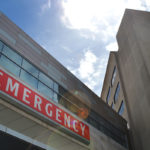 A view from below of a building bearing a red sign with the word “EMERGENCY” prominently displayed.