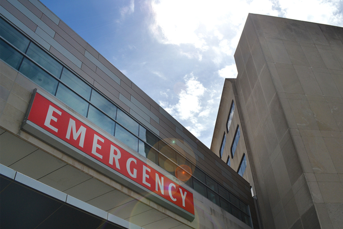 A view from below of a building bearing a red sign with the word “EMERGENCY” prominently displayed.