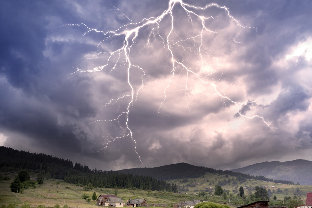 A thunderstorm and lightning flashes in the sky over hills with several houses.