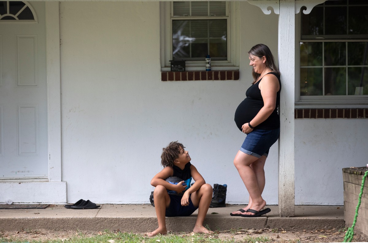 Jessica Wright stands outside a home and looks down at her son, who is seated.