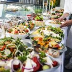 A waiter serves a large buffet table full of food.