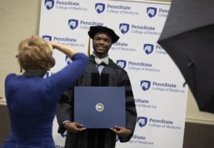A man smiles for a photo as he holds his diploma.