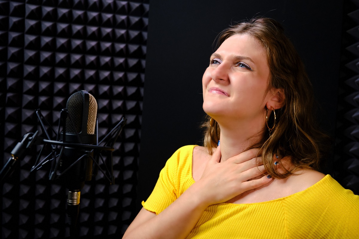 A young woman holds her throat while standing near a microphone.