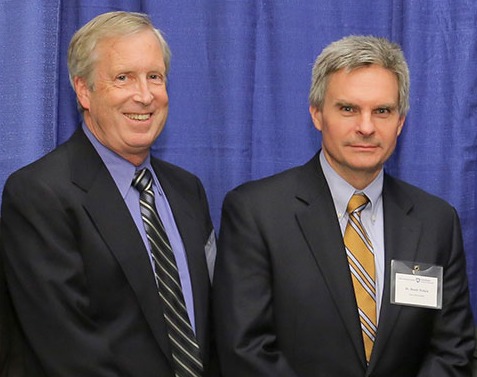 Barry Fell and Randy Haluck are seen wearing suits and standing in front of a professional photo background