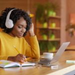 A woman sits in front of a computer with headphones on.