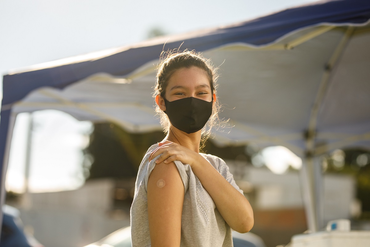 A girl in a mask shows the bandage where she received the vaccine on her arm.