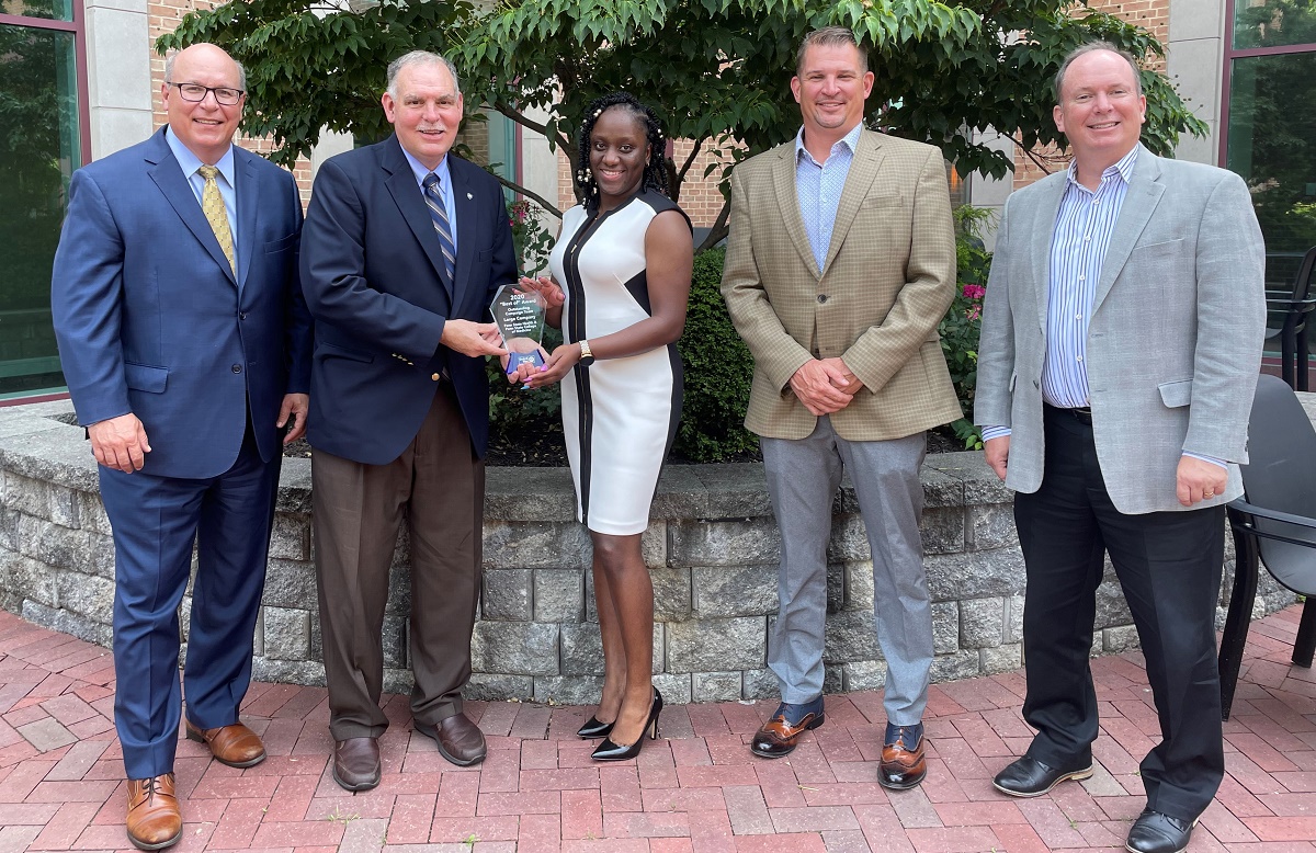 Four men and one woman stand in a courtyard and smile at the camera. From left are Steve Massini, Penn State Health CEO; Jim George, Penn State Health director of community relations; Michelle Phillips, United Way of the Capital Region (UWCR) campaign manager; Anthony Worrall, Reynolds Restoration Services president and UWCR campaign vice chair; and Tim Fatzinger, UWCR president and CEO, celebrate the Outstanding Campaign Team Award. Jim George and Michelle Phillips are holding a Plexiglas trophy engraved with a United Way award won by Penn State Health and Penn State College of Medicine.