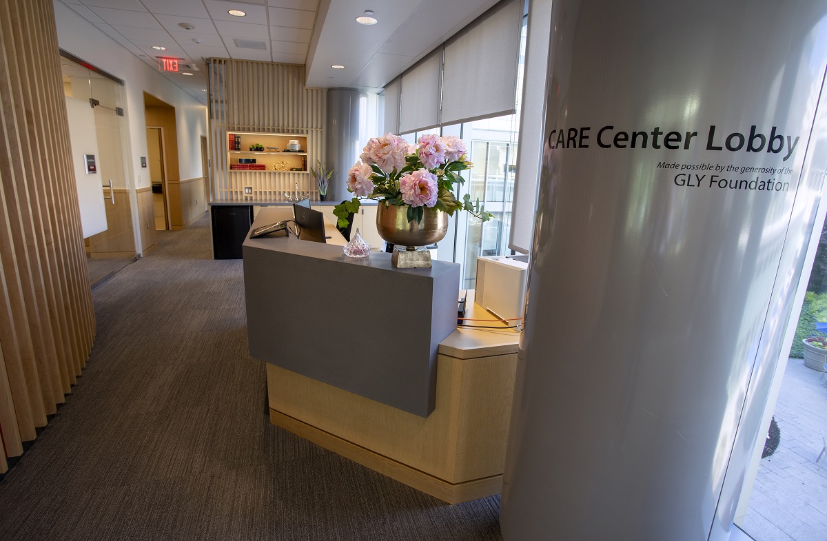 The lobby of the Cancer Assistance and Resource Education Center in Penn State Cancer Institute shows a reception desk with a bowl of flowers on it, a column on the right with the words “CARE Center Lobby” on it and a wall with slats on the left.