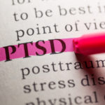 Close-up of the acronym “PTSD” in a book being highlighted by a marker.