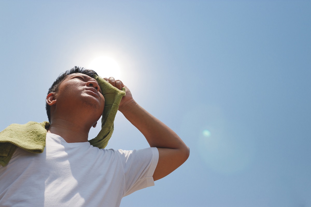 A man holds a towel to his forehead as the sun blazes overhead.