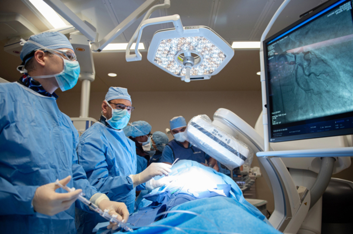 Physicians dressed in scrubs perform a cardiac catherization.