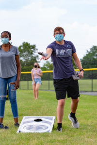 Two students wearing surgical masks throw beanbags during lawn game.