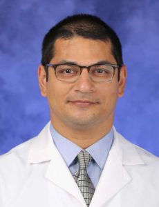 Dr. Moses Mathur, wearing a white coat, poses for a professional headshot.