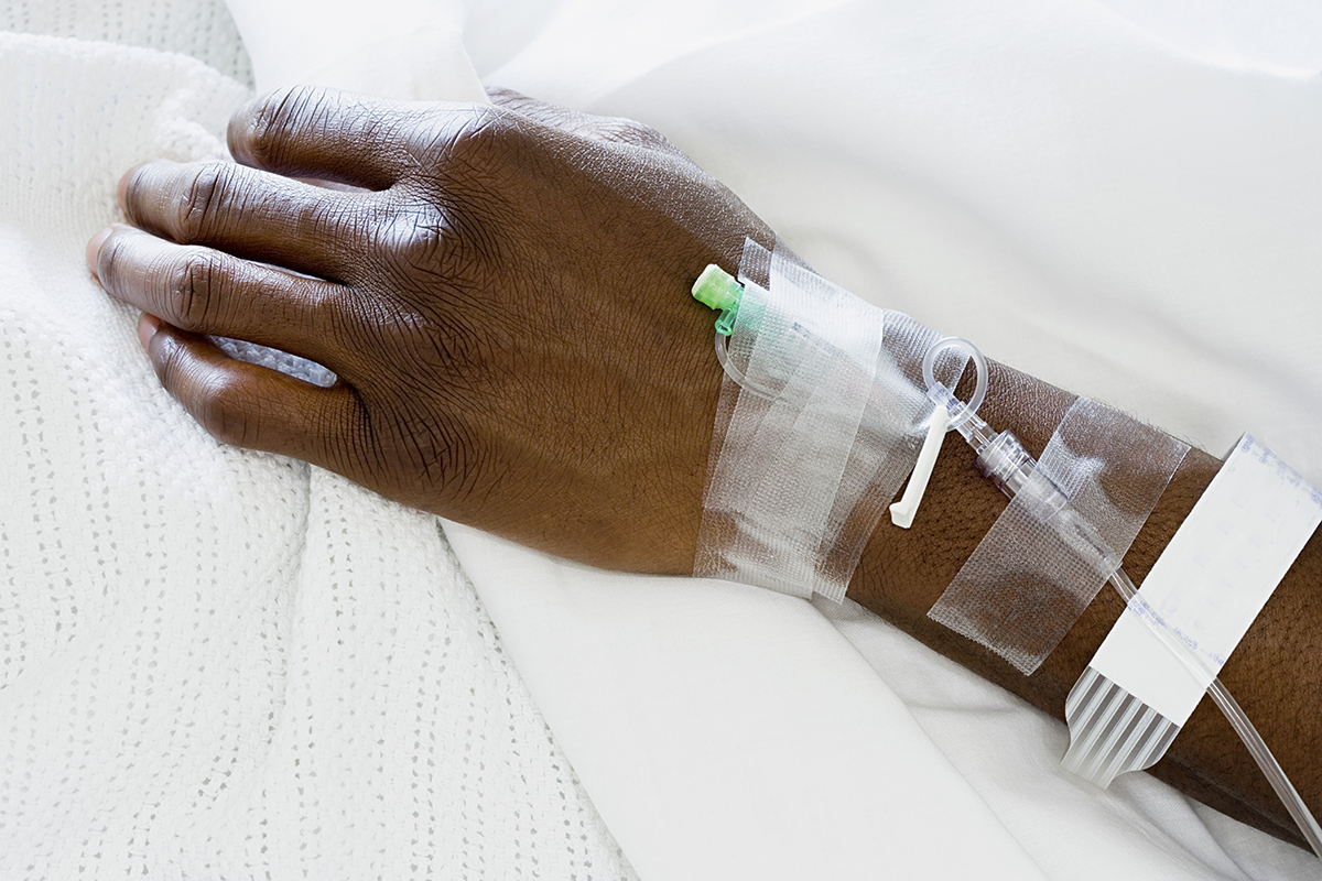 Close-up of a wrist and hand into which an IV line is inserted. Medical tape is on the arm, securing the line in place.