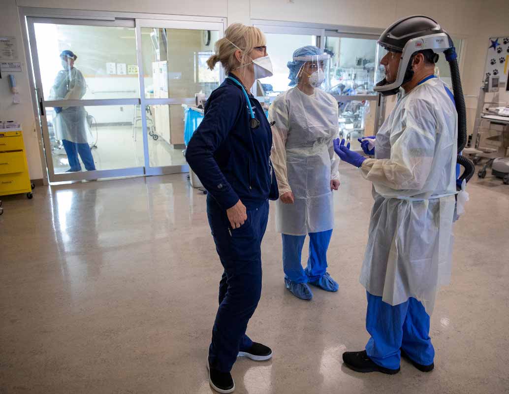 Un equipo de atención vestido con equipo de protección personal completo se reúne fuera de la habitación de un paciente del hospital