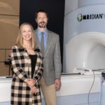 A man and woman stand in front of a Magnetic Resonance Imaging-guided linear accelerator.
