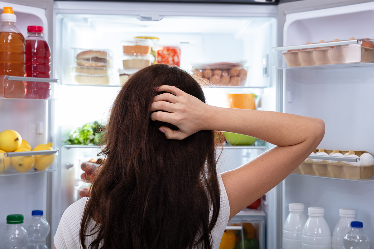 Confused Woman Searching For Food In An Open Refrigerator
