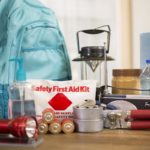 Sitting on a table are the makings of a safety kit: a backpack, lantern, bottles of water, first aid kit, flashlight, batteries, can opener, radio and other items.