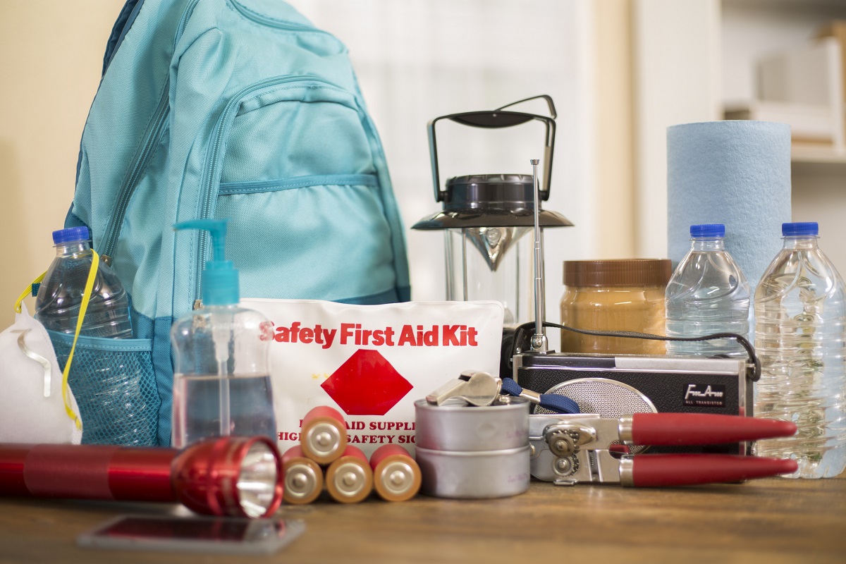 Sitting on a table are the makings of a safety kit: a backpack, lantern, bottles of water, first aid kit, flashlight, batteries, can opener, radio and other items.