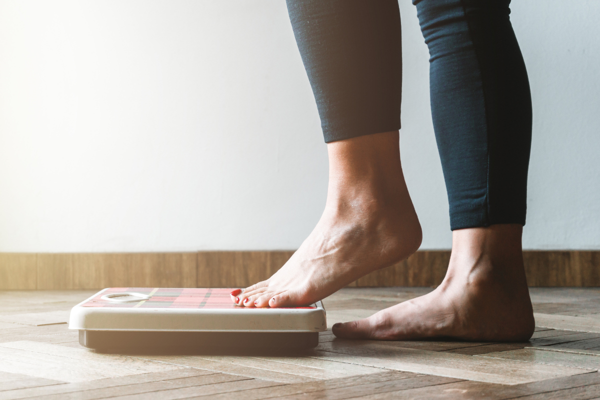 A woman steps onto a bathroom scale with her left foot first. Image is from the knees down.