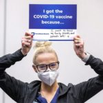 A woman holds a sign over his head that says, “I got the vaccine because I want to keep my family, friends and patients safe.”