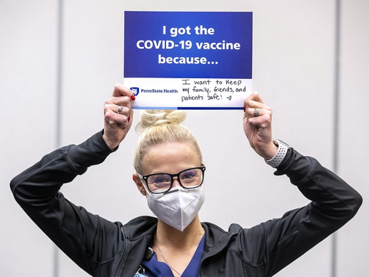 A woman holds a sign over his head that says, “I got the vaccine because I want to keep my family, friends and patients safe.”
