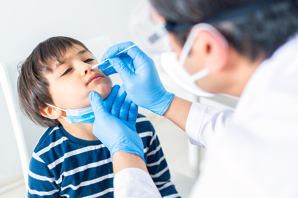 A doctor tests a young boy for COVID-19 via nasal swab.