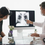 A patient and a doctor discuss cancer prognosis while viewing a chest x-ray.