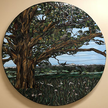 Glass mosaic on browns and greens in front of a blue sky forming a large tree within a circle 