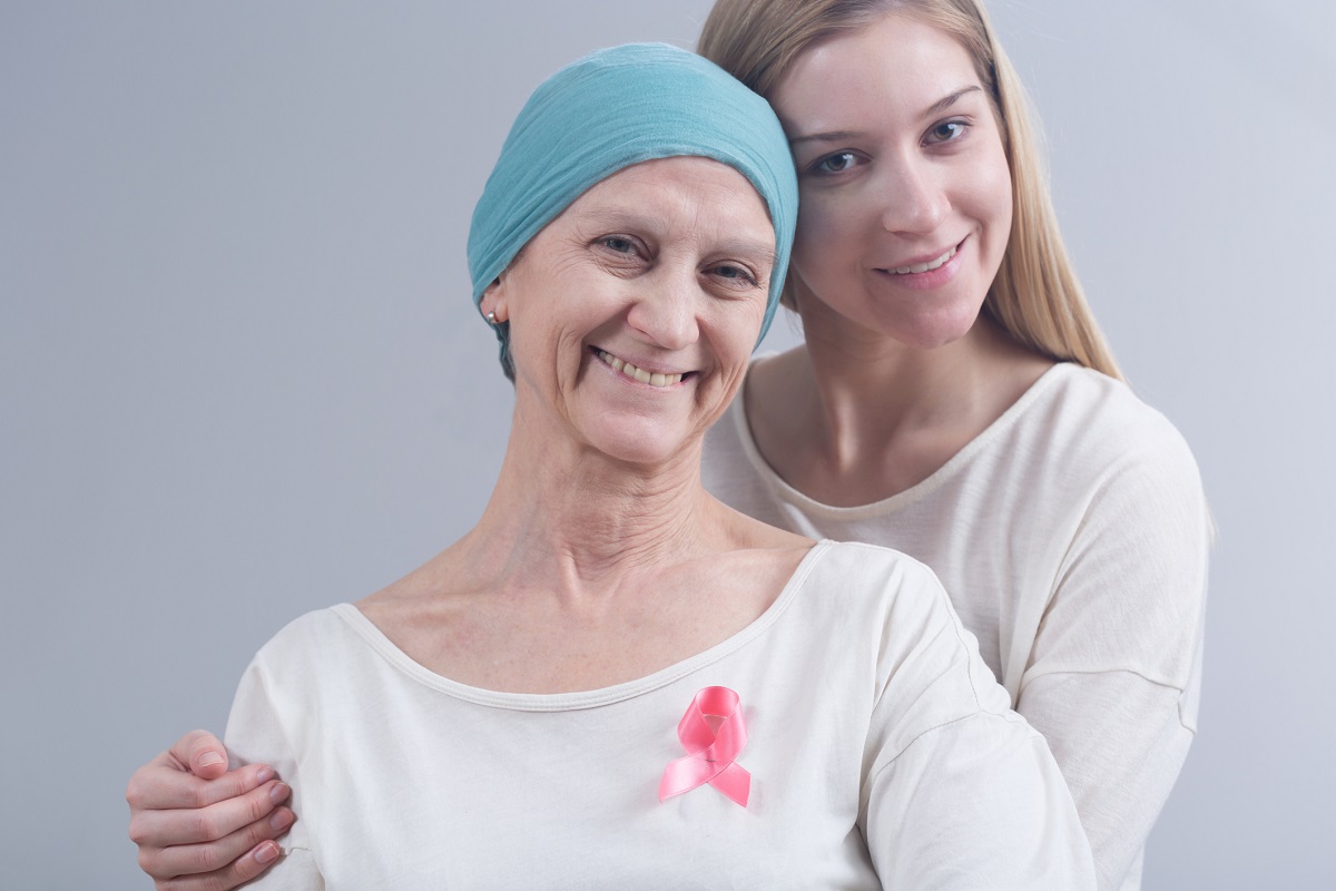 A woman with breast cancer poses with her daughter. Both are smiling.
