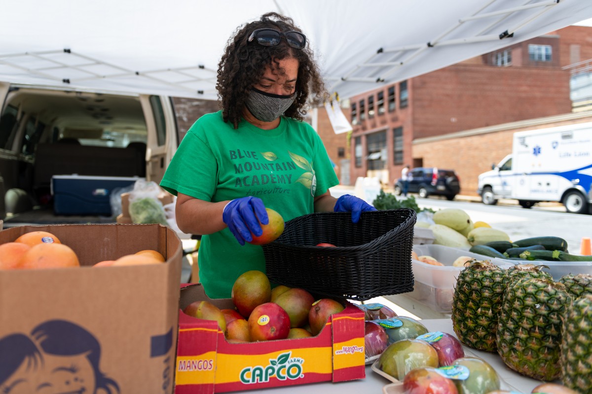 Christina Houston, miembro del personal de Blue Mountain Academy, organiza frutas y verduras para venta en el puesto de agricultura del campus del centro de Penn State Health St. Joseph.