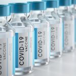A row of vaccine vials displays labels indicating they are for COVID-19.