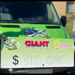 Nipsey and Jen Shade from The People’s Morning Show on WQXA 105.7 The X stand in front of a station vehicle, holding a sign that has the amount $310,095 on it.