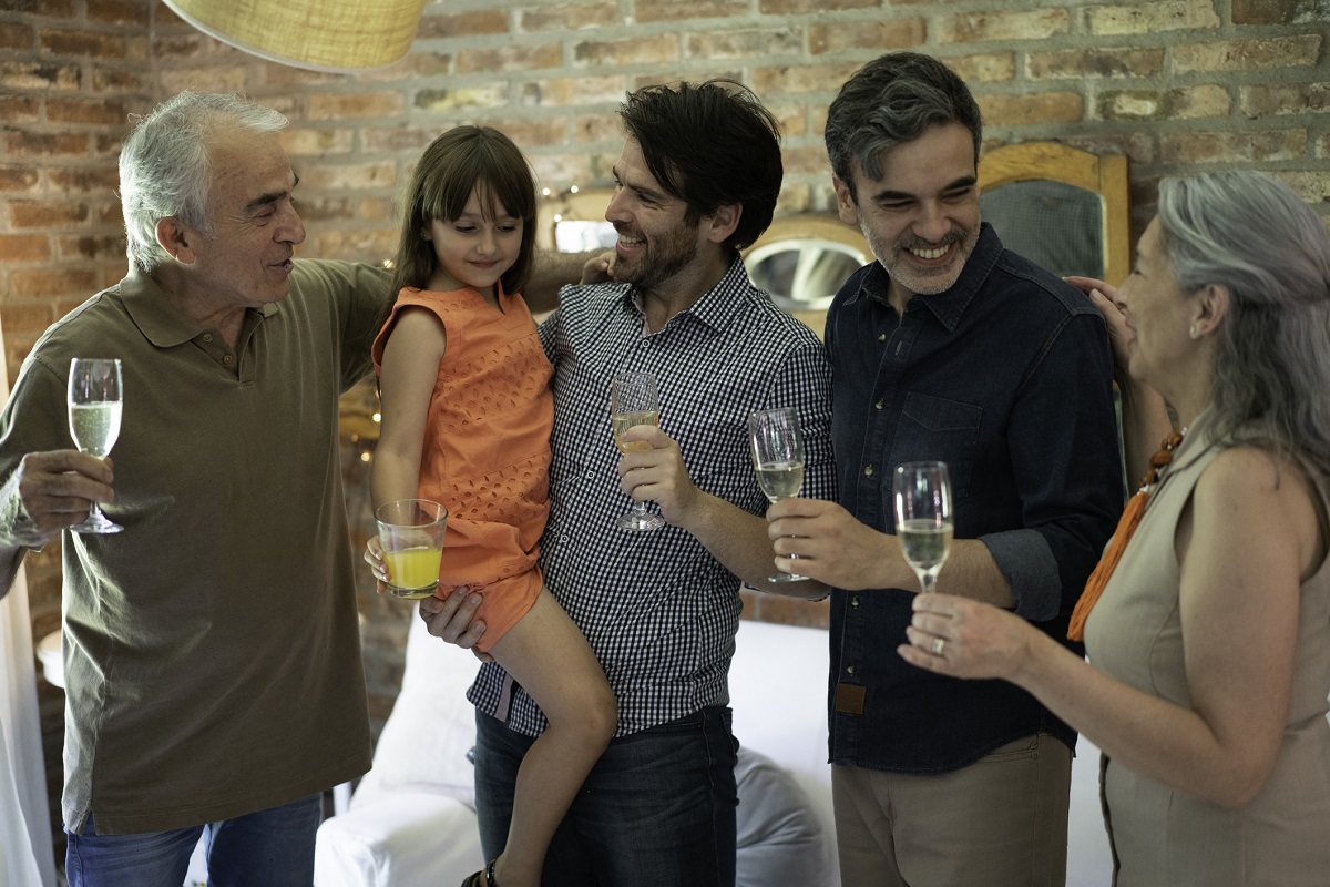 A family raises champagne flutes for a holiday. There are four adults and a child. The child holds a glass of juice.