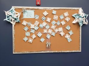 A bulletin board in an office features a construction paper tree covered in snowflake cut outs.