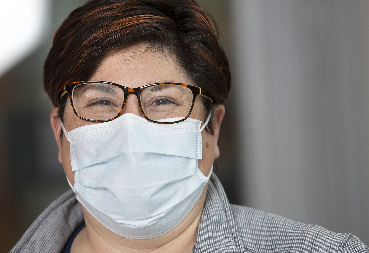 Woman with short hair, glasses and a surgical mask, smiling.