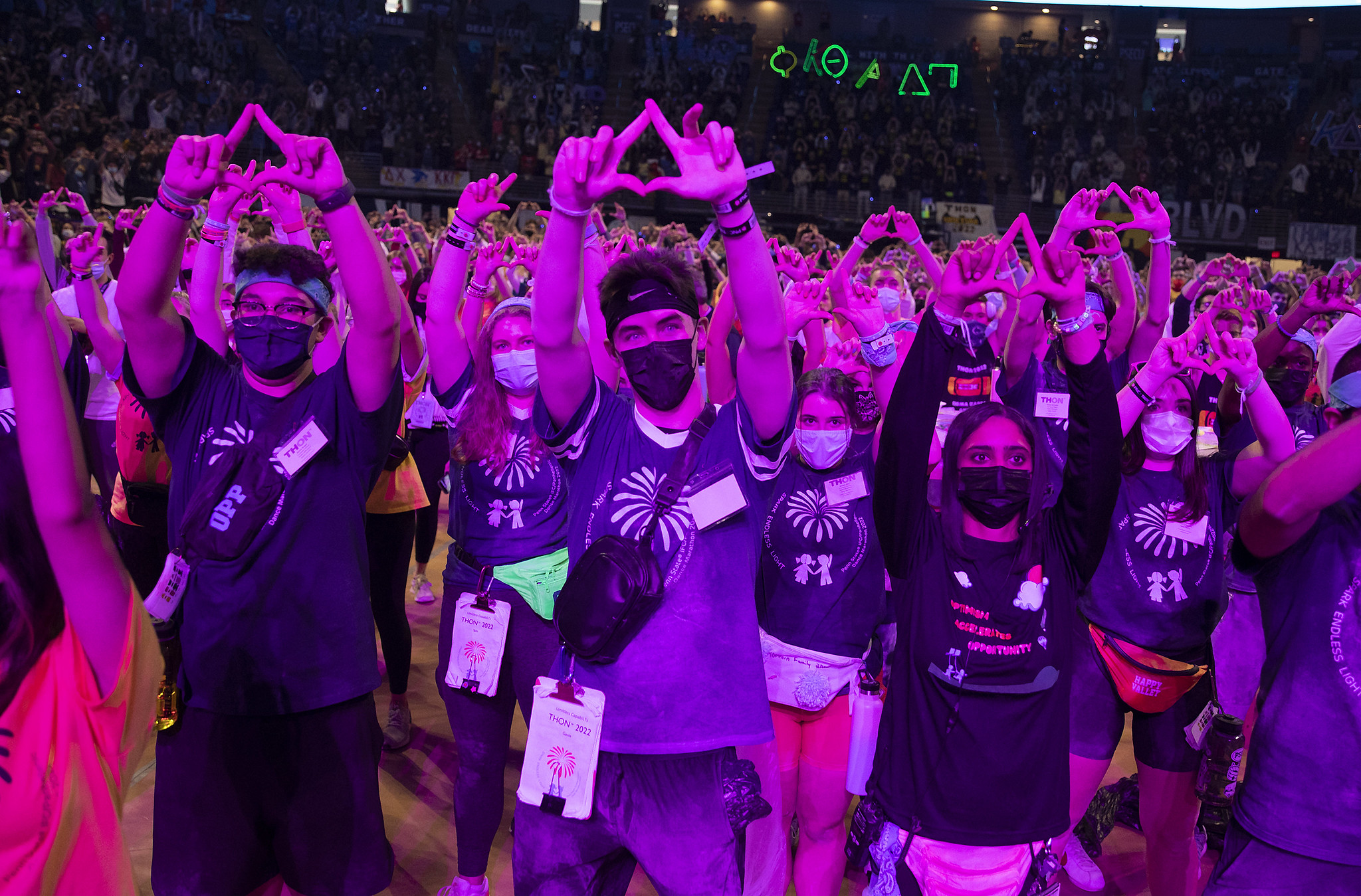 Several dancers at THON 2022 stand on the dance floor with their hands raised in the air, making diamond shapes with their fingers.