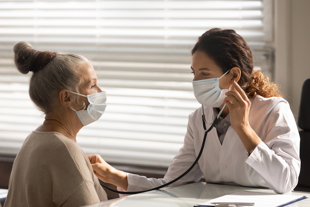 A doctor in a surgical mask hold a stethoscope as she listens to a patient’s heart.