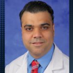 Photo of male doctor wearing physician white coat, shirt and tie. The words “Muhammad Fahad Khalid, MD Chief, Division of Hospital Medicine, Physician of the Month” appear beside the photo, which includes the Penn State Nittany lion